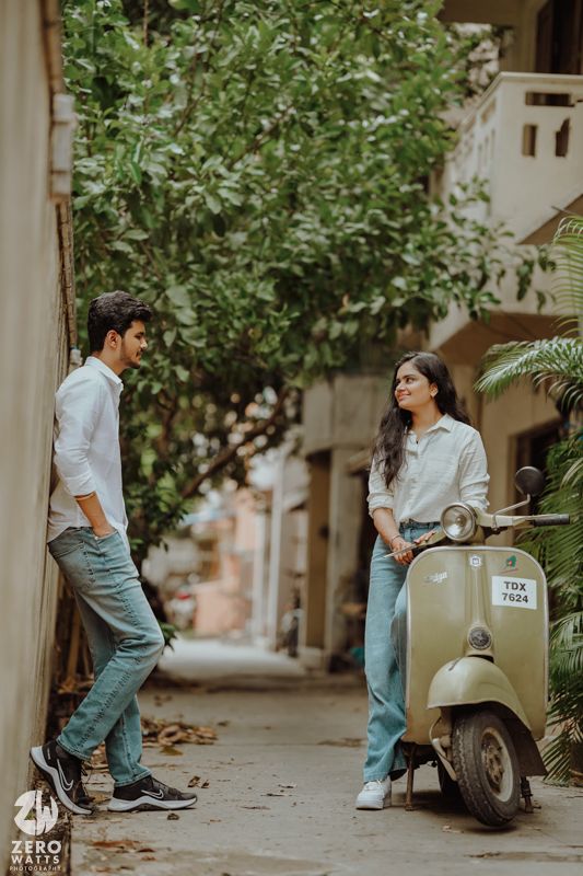 Romantic photoshoot with couple and classic Vespa scooter on tree-lined street.