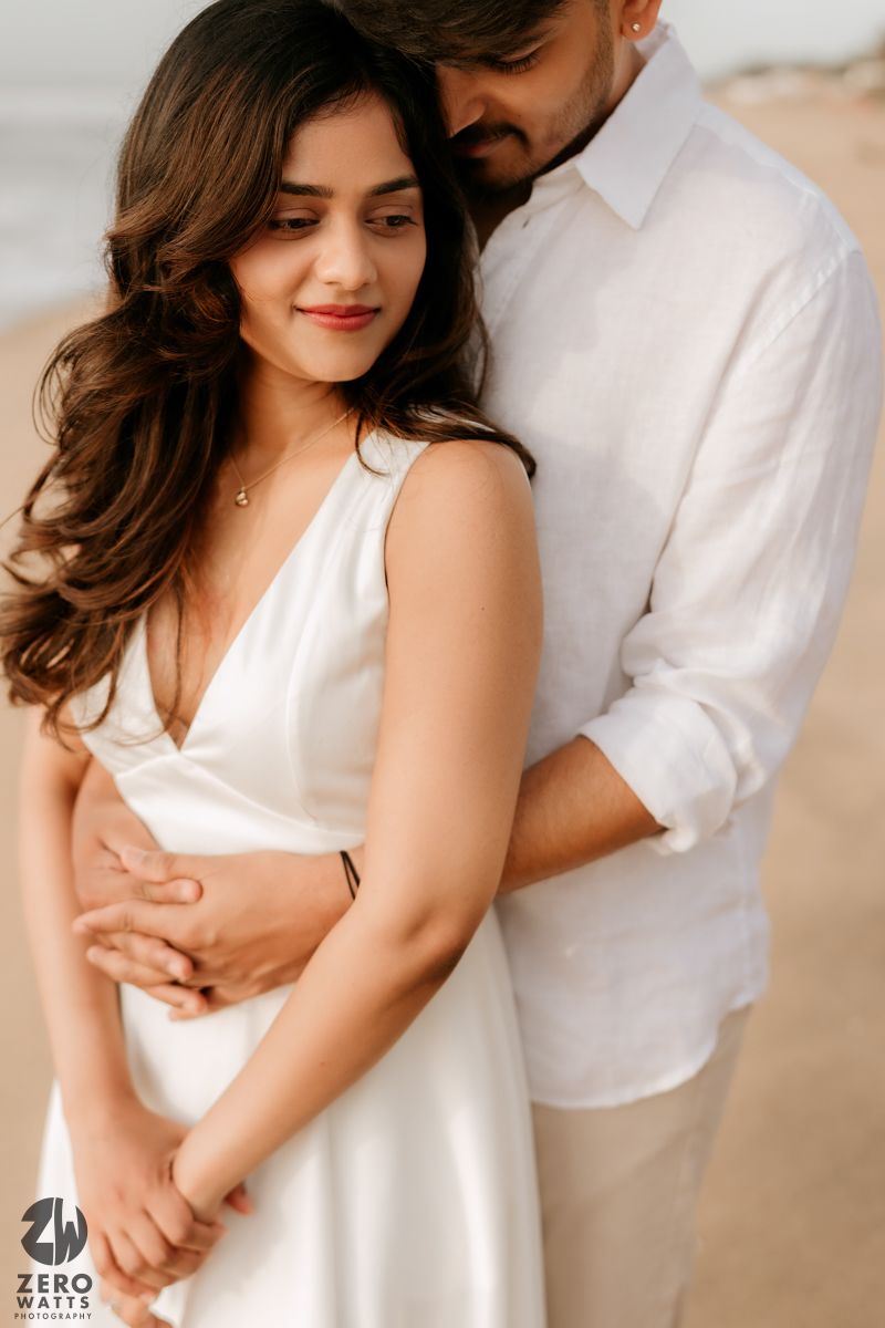 Romantic couple in white attire embracing tenderly against light background during intimate photoshoot.