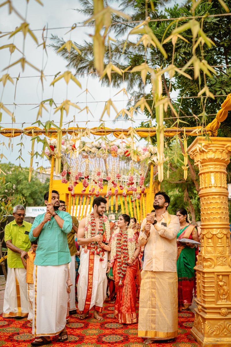 Traditional Indian wedding ceremony setup with floral decorations, gold pillars and ethnic attire under a decorated mandap canopy.