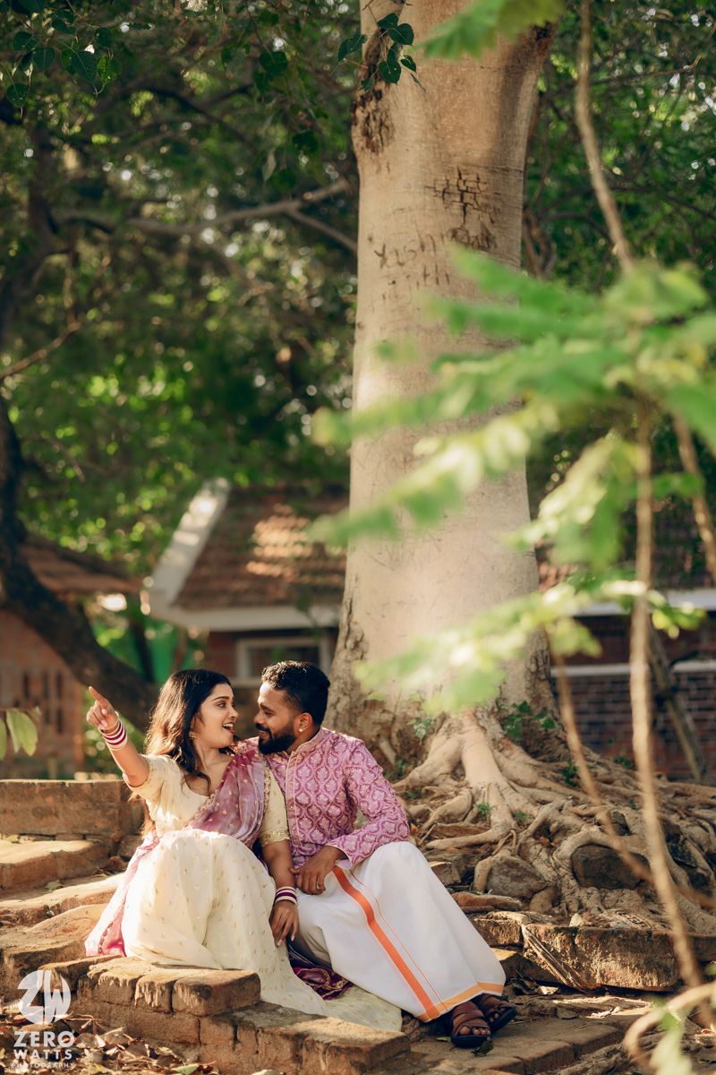 Romantic couple laughing together while seated beneath a majestic tree in traditional dress.