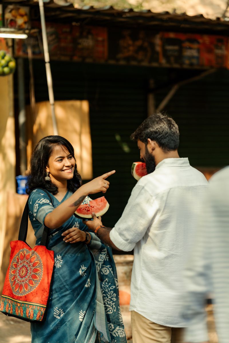 A couple shares fresh watermelon while enjoying a casual moment together on the street.