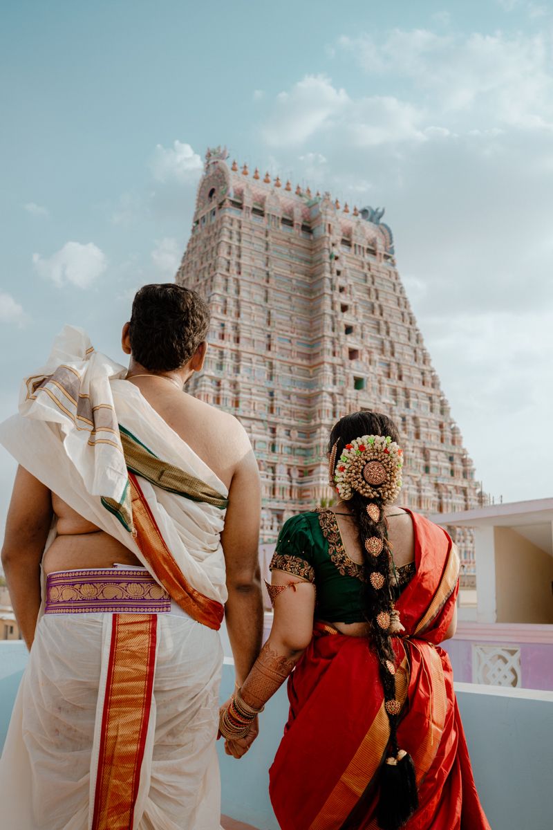A couple in traditional South Indian attire standing before the grand Gopuram tower of a Hindu temple.