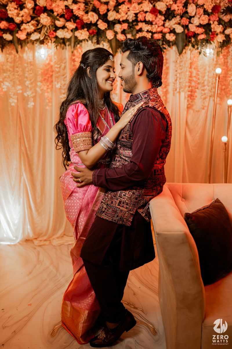 A couple embraces during an intimate moment at a wedding celebration with coral floral decor and warm lighting.
