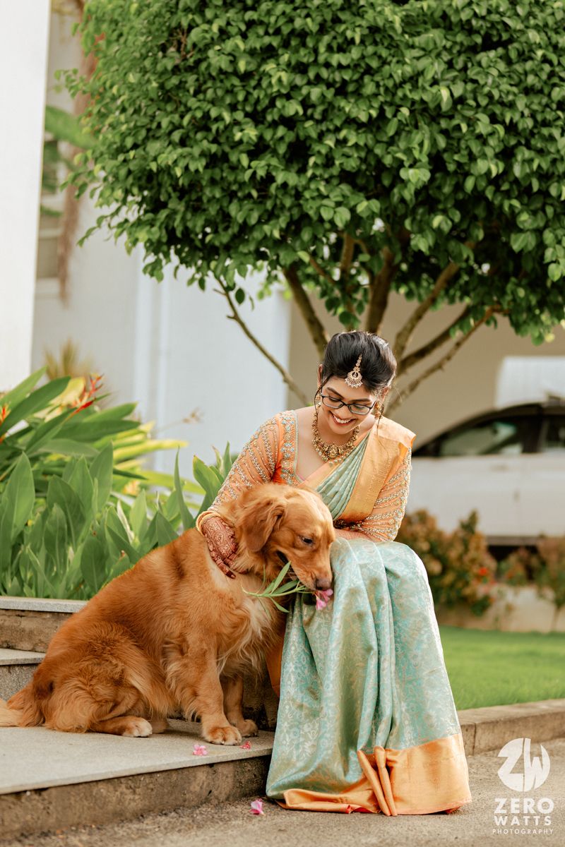 Golden Retriever sits on garden steps next to someone in traditional Indian attire beneath a lush green tree.