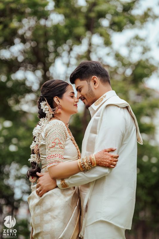 A romantic couple in traditional South Asian wedding attire embrace in a garden setting with bokeh effect.