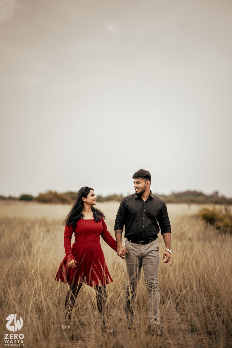 A couple walking through tall grass in a field during golden hour.