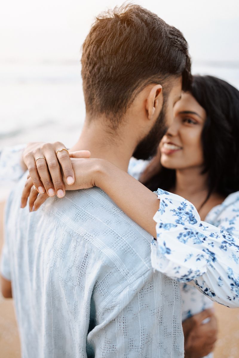 Romantic couple embracing at sunset with woman in blue floral dress resting hands on partner's shoulders.