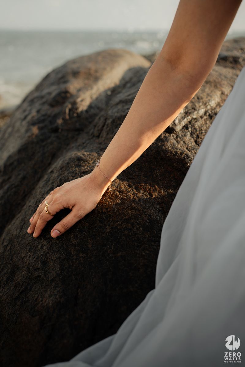 Close-up of hand touching rough coastal rock surface against ocean backdrop.