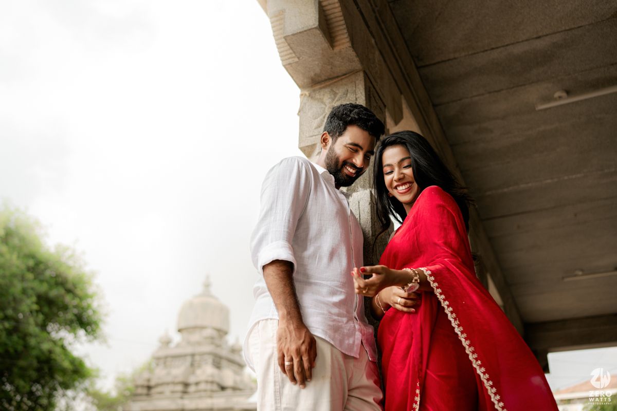 A romantic couple moment captured under temple architecture with white dome visible in background.