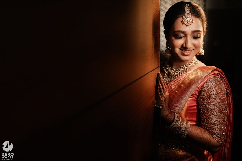 Traditional Indian bride wearing red silk saree and ornate jewelry smiles elegantly against dark background.