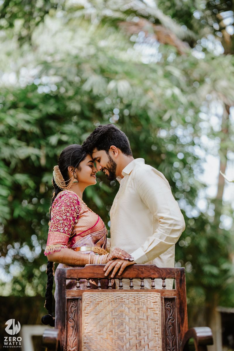 A romantic moment captured between a couple in traditional Indian wedding attire against a leafy backdrop.