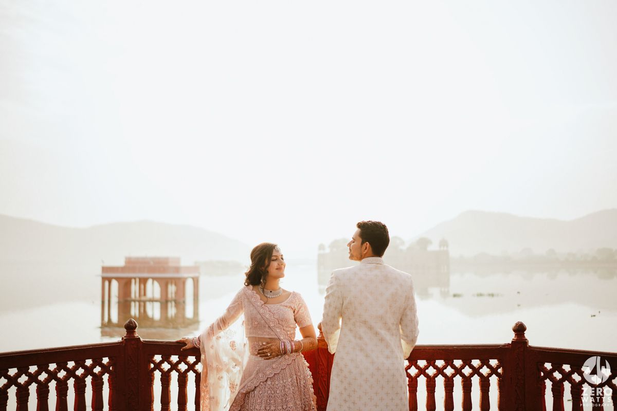 Couple in traditional Indian attire admire the lake view from an ornate balcony during golden hour.