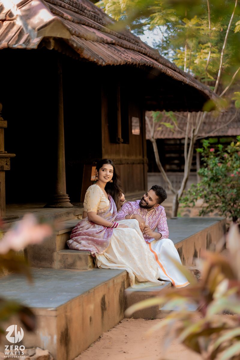 A couple in traditional attire relaxing on the veranda of a rustic Kerala-style home.