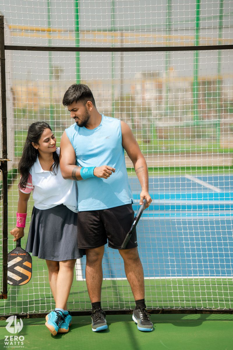 Couple in sports attire standing together on pickleball court holding their paddles.