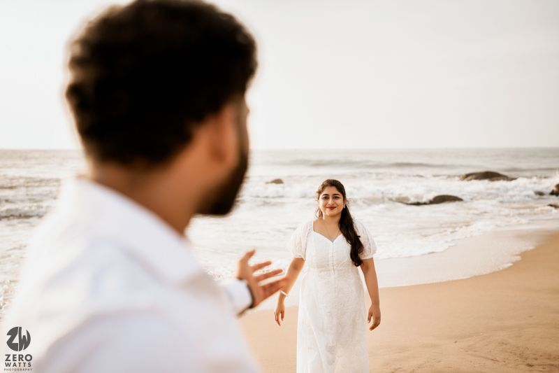 A beach photoshoot scene with two people in white outfits captured in candid interaction.