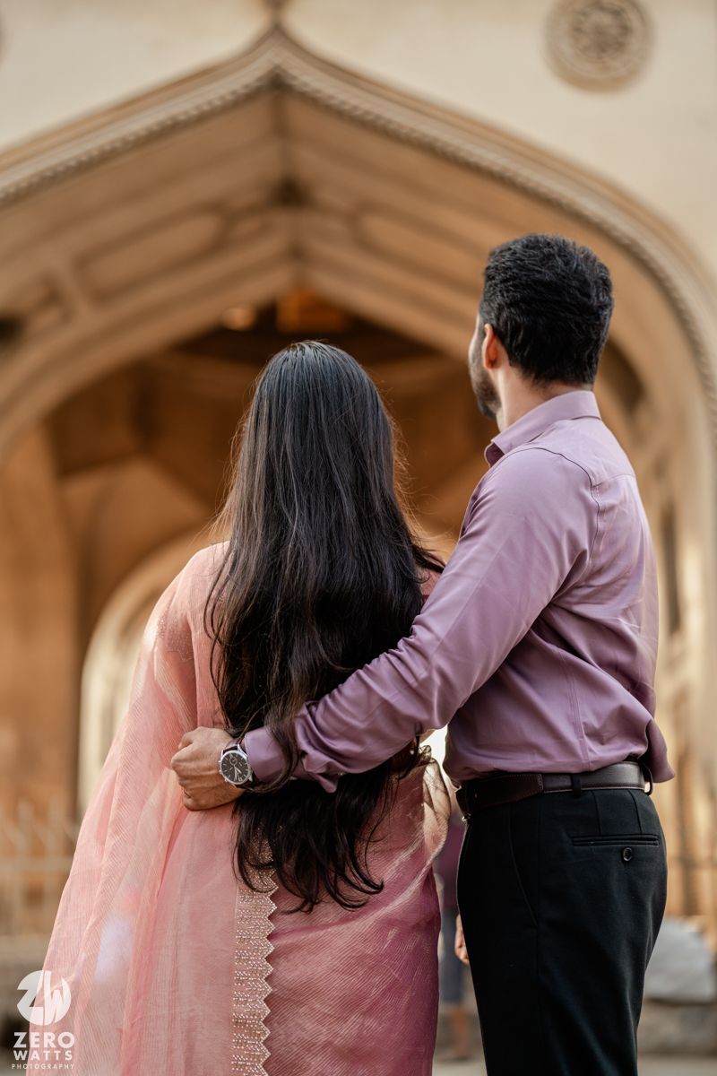 A couple embraces in front of ornate architectural archway in traditional Indian attire.