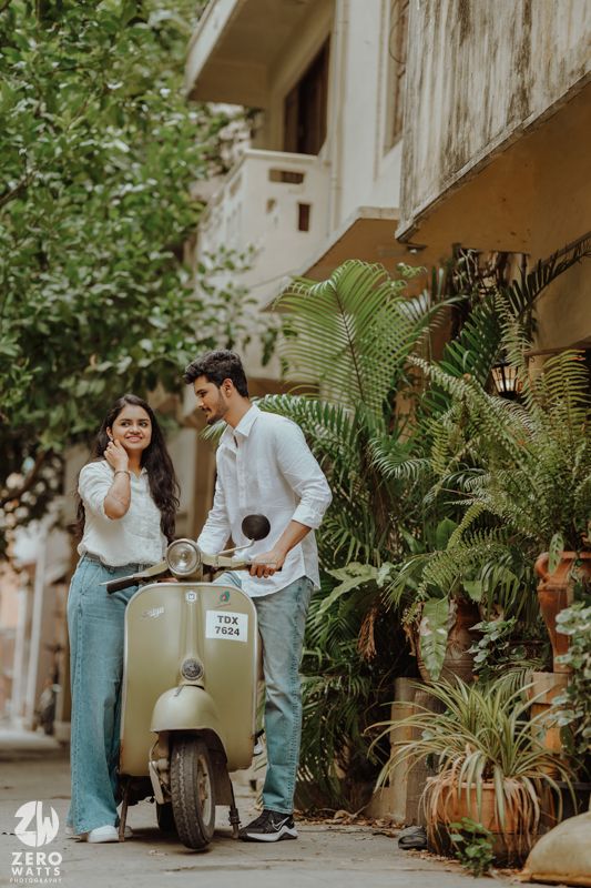Casual couple sharing moment next to mint green Vespa scooter surrounded by plants.