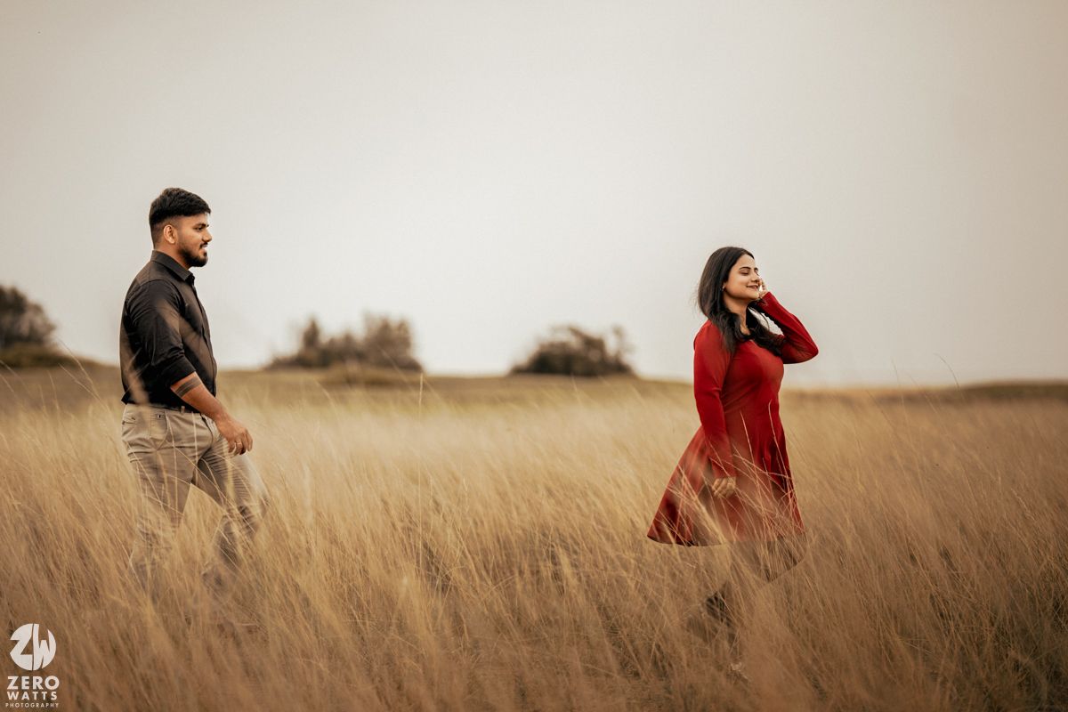 Romantic couple standing apart in a golden grass field during sunset.