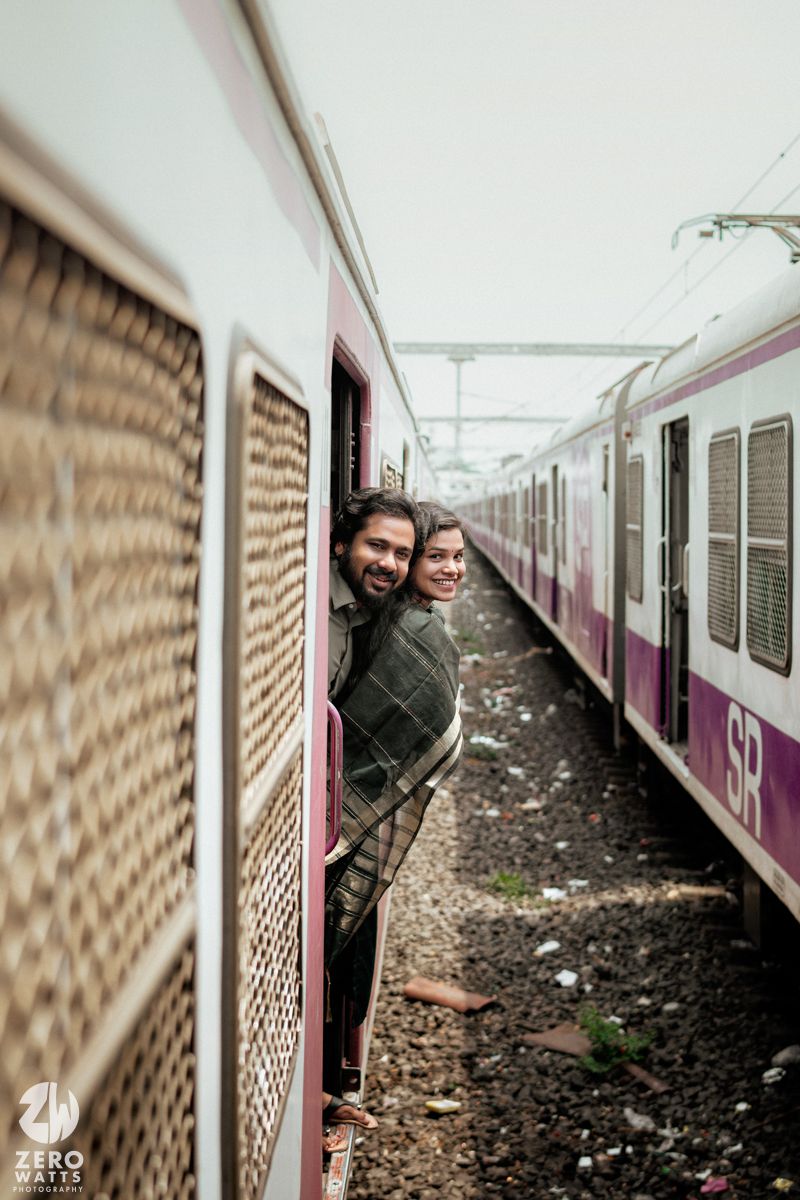 A playful couple peeks out from a train door while traveling together.
