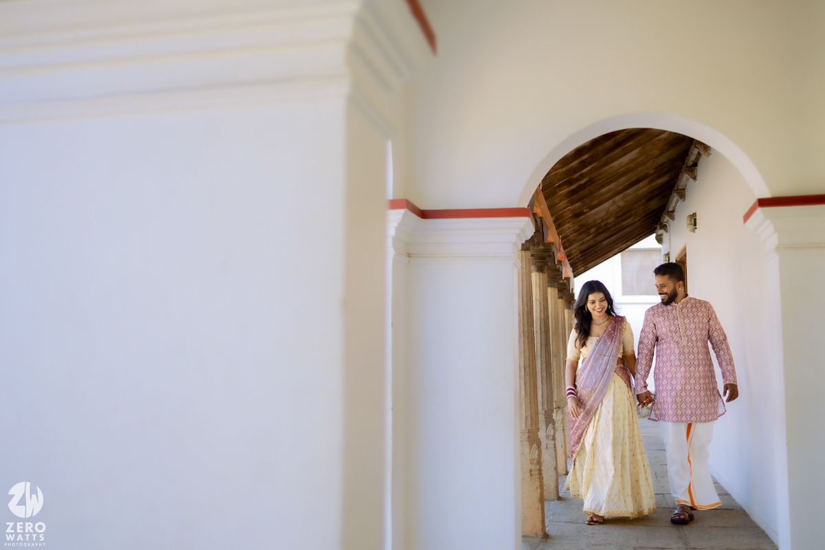 A couple walking hand in hand through a white corridor with a decorative red stripe along the wall.