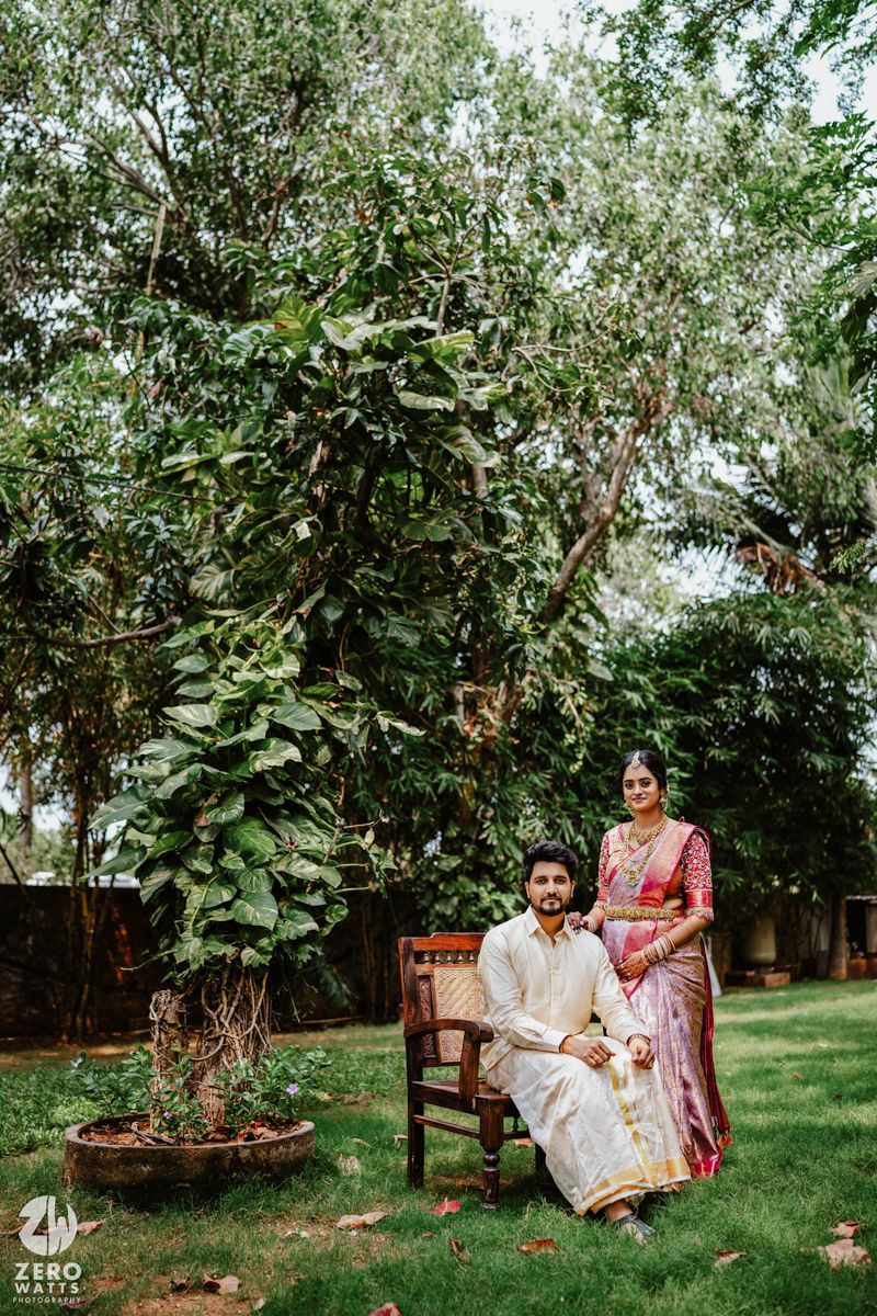 Traditional South Indian couple posing in garden setting with wooden chair.