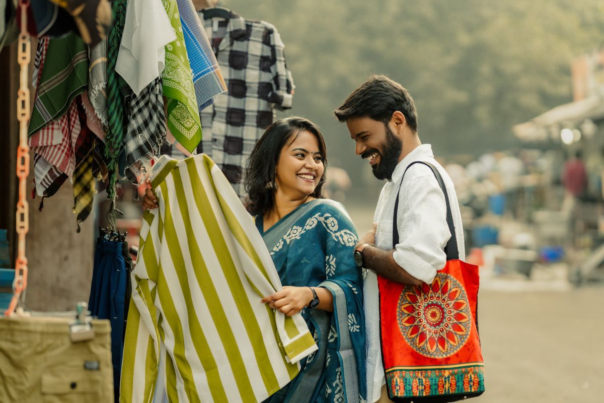 Couple shopping at outdoor market looking at colorful textiles and fabrics with bags in hand.