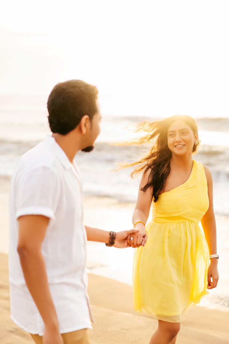 Couple holding hands and smiling during golden hour photoshoot on a sunset beach.