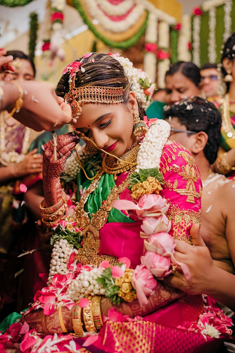 Traditional South Indian bride in pink saree adorned with ornate jewelry during wedding ritual.