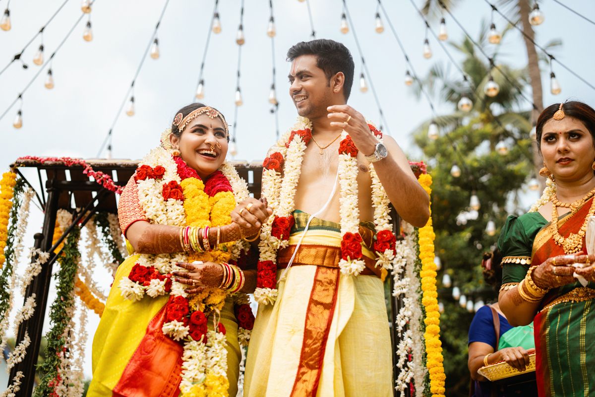 Traditional South Indian wedding ceremony with couple in traditional attire and floral garlands under decorated mandap.