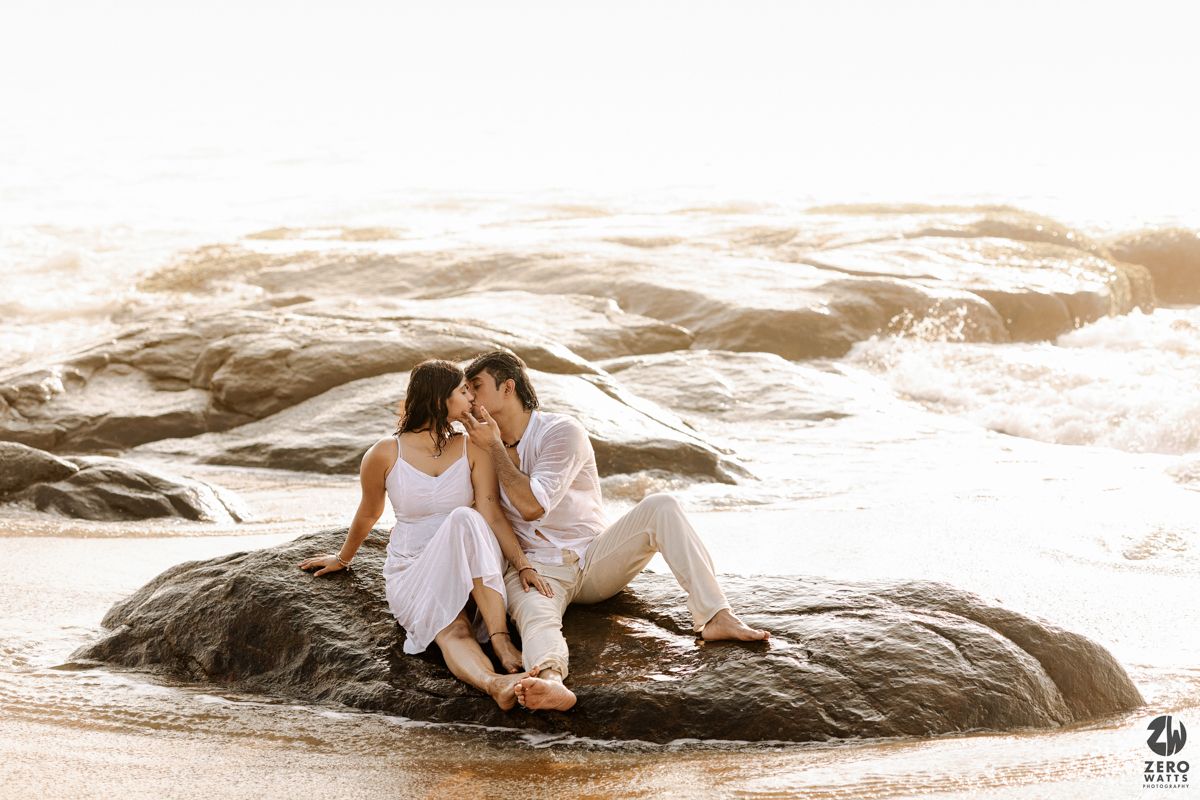 Romantic couple sitting together on seaside rocks during sunset photoshoot.
