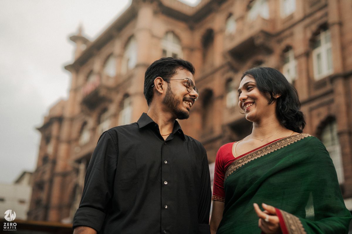 Couple in traditional Indian attire sharing a moment against historic architecture.