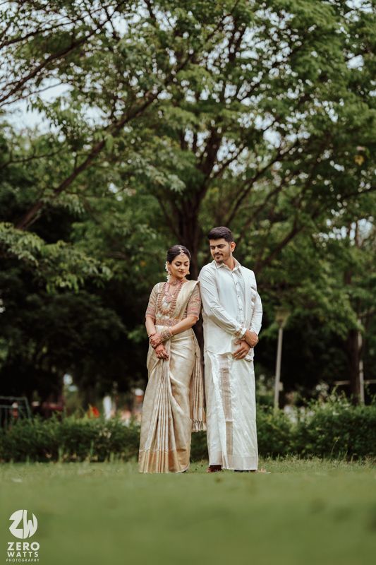 A couple in traditional Indian wedding attire shares an intimate moment in a lush garden setting.