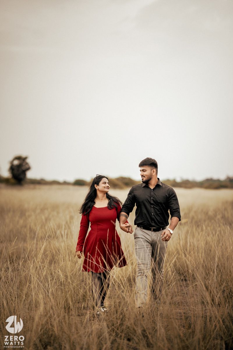Two people in formal wear sharing a romantic moment in a rustic field setting.