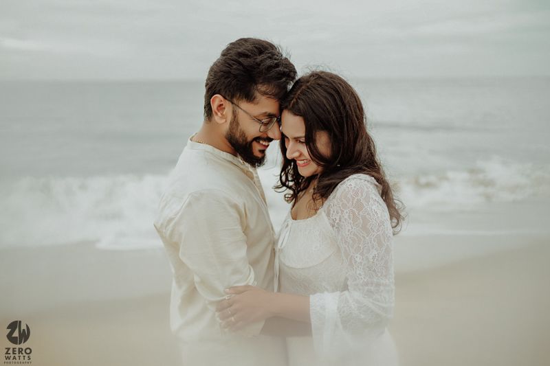 A romantic beach photoshoot featuring an intimate moment against grey ocean backdrop.
