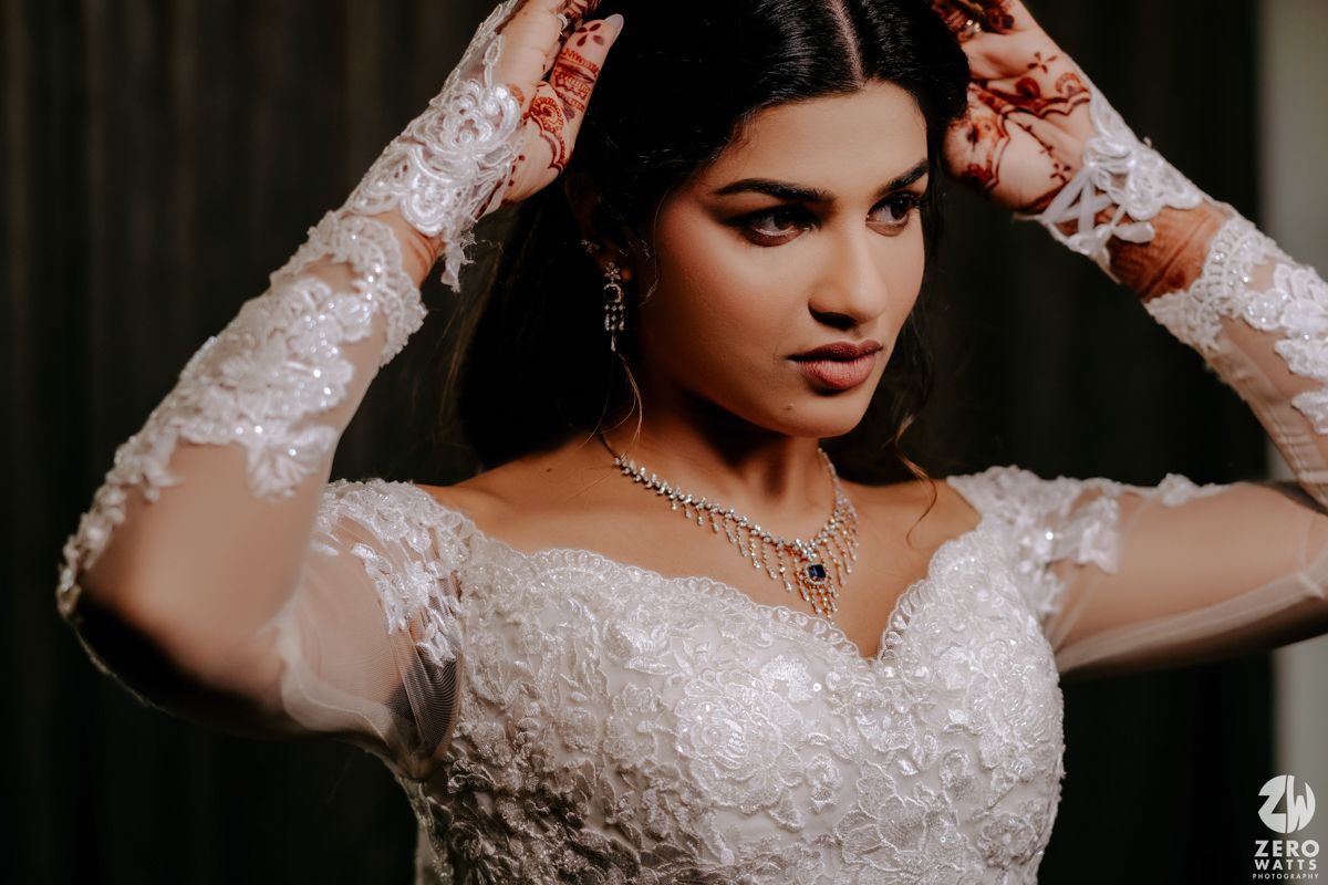 A person in a white lace wedding dress with long sleeves and silver jewelry in a dramatic portrait setting.