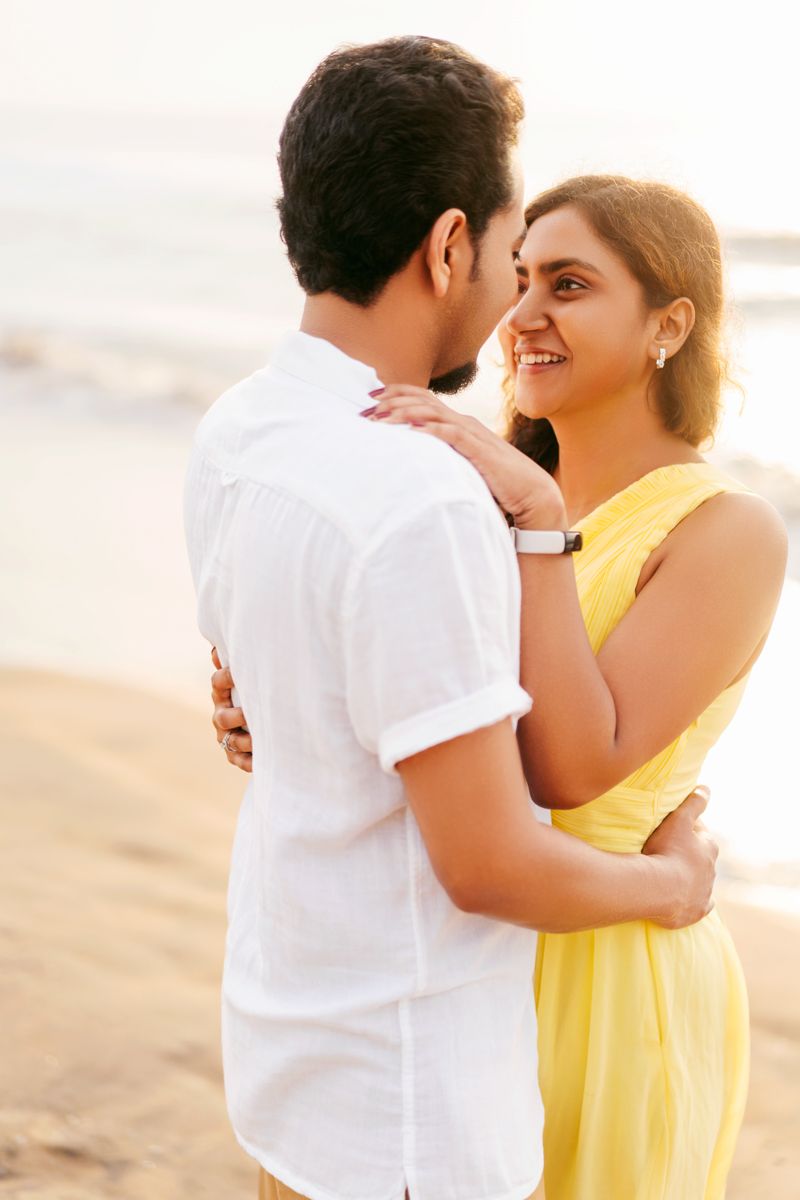 Intimate beach moment between couple in white and yellow attire at sunset.