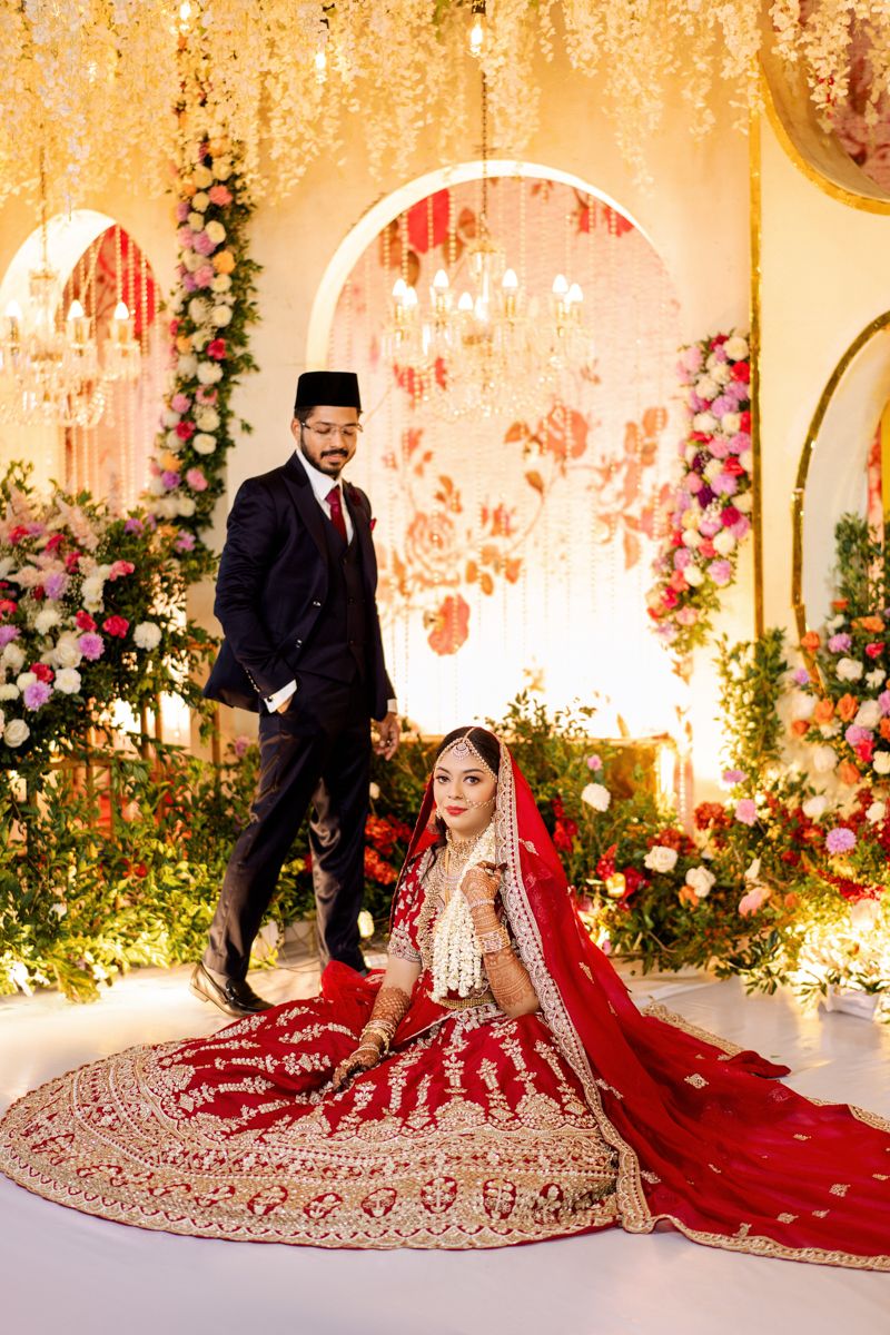 Elegant wedding venue decorated with floral arches and pink roses features a couple in traditional formal attire.