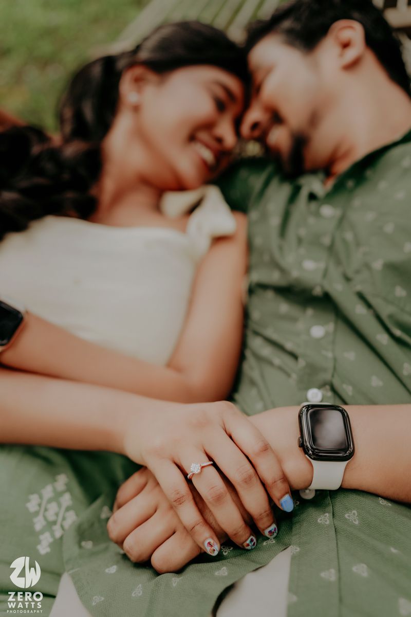 Close-up of hands with an engagement ring and Apple watch, showing intimacy between a couple lying outdoors.