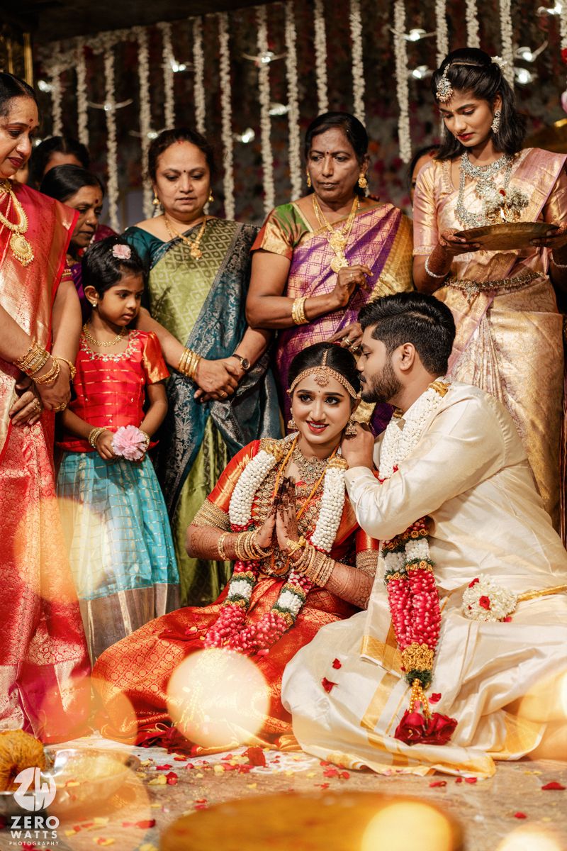 Traditional South Indian wedding ceremony with guests in colorful silk sarees gathered around couple during rituals.
