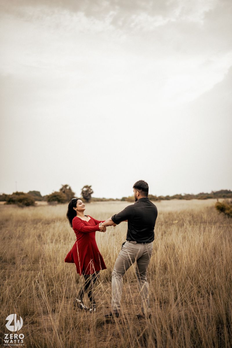 A couple poses playfully in a golden grass field during sunset.