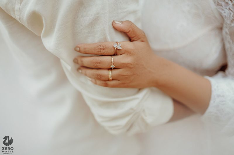 Close-up of hand wearing engagement rings against white fabric background.