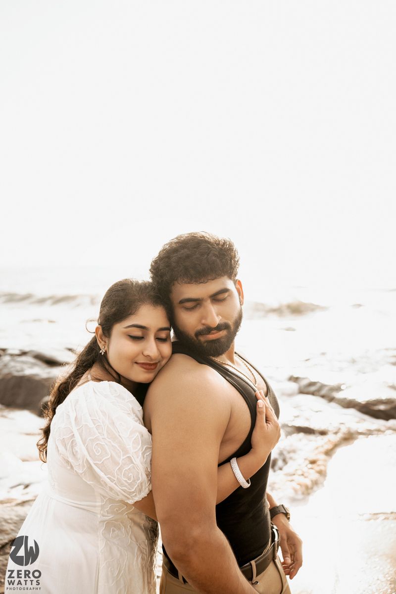 Intimate seaside photoshoot shows couple embracing with sun-lit backdrop.