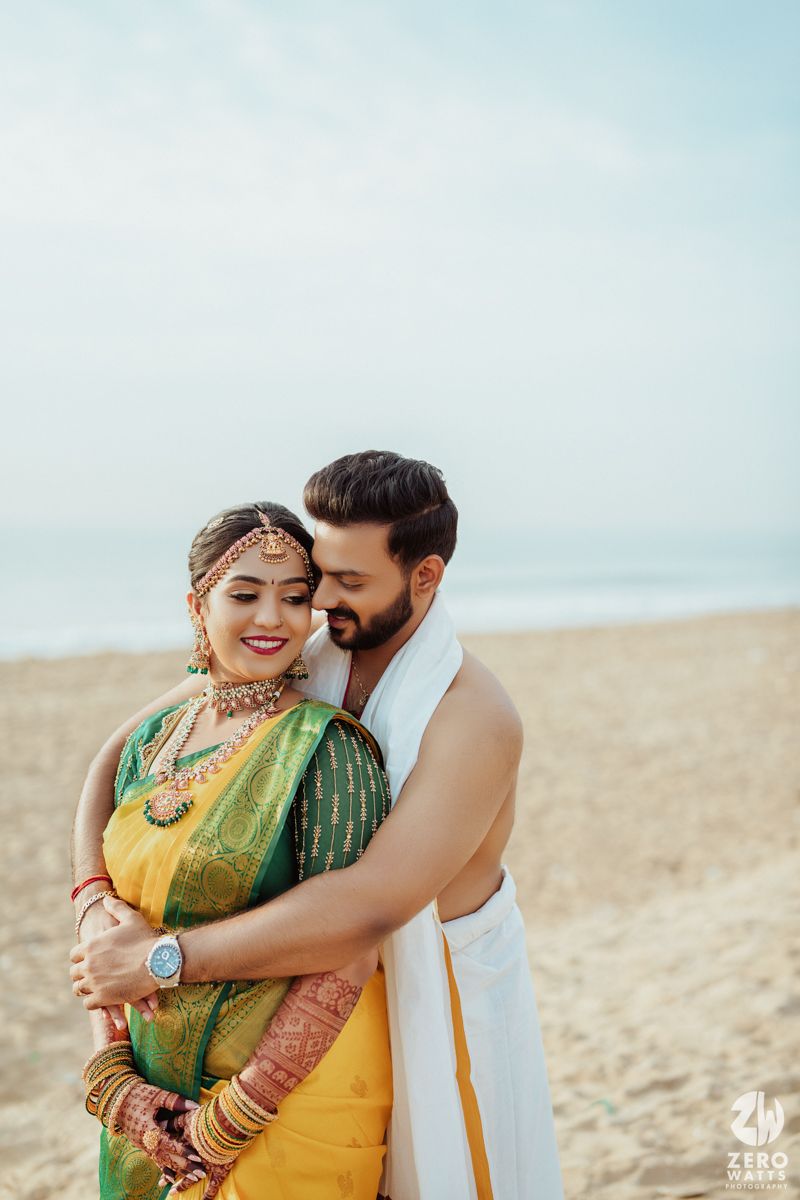 Couple in traditional South Indian wedding attire embracing on a beach.