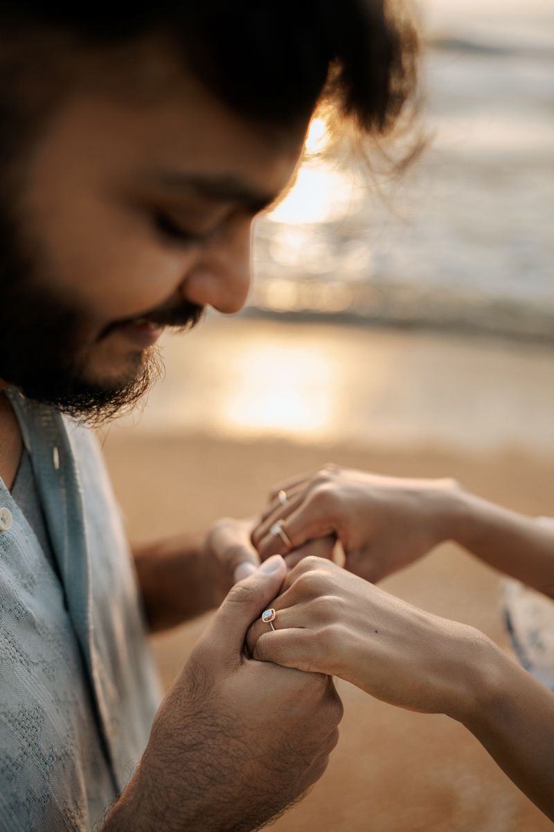 Close-up of hands exchanging rings during intimate beach proposal moment.