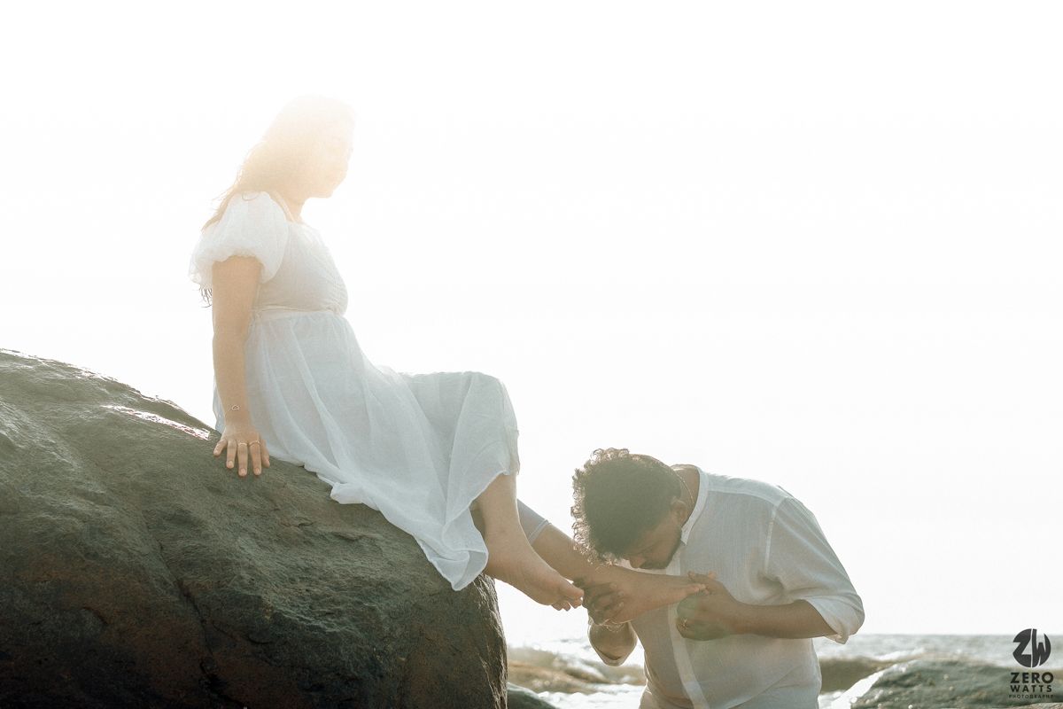 A couple poses intimately on seaside rocks during a dreamy backlit sunset photo session.