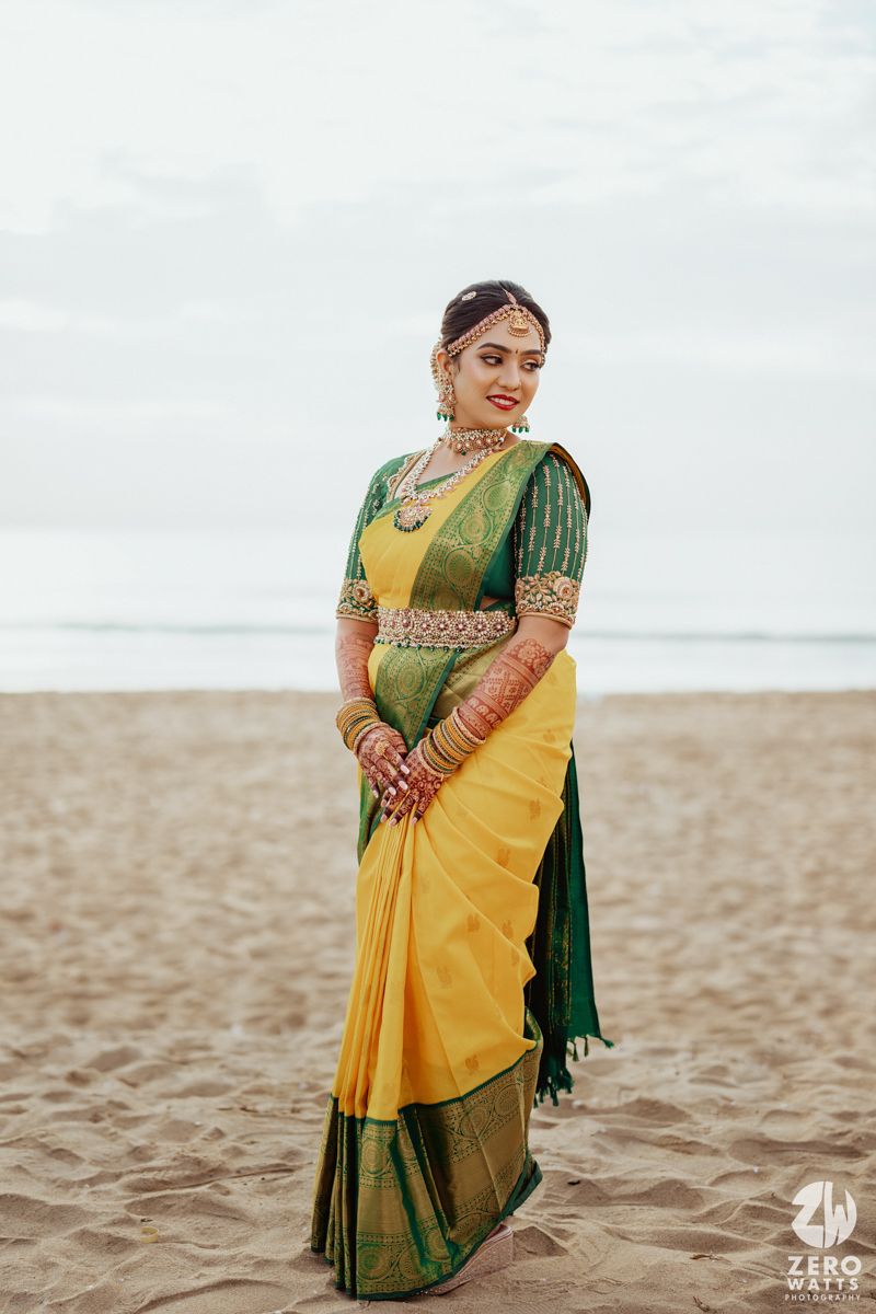 Traditional South Indian bridal attire featuring yellow and green silk saree with ornate jewelry on a sandy beach.