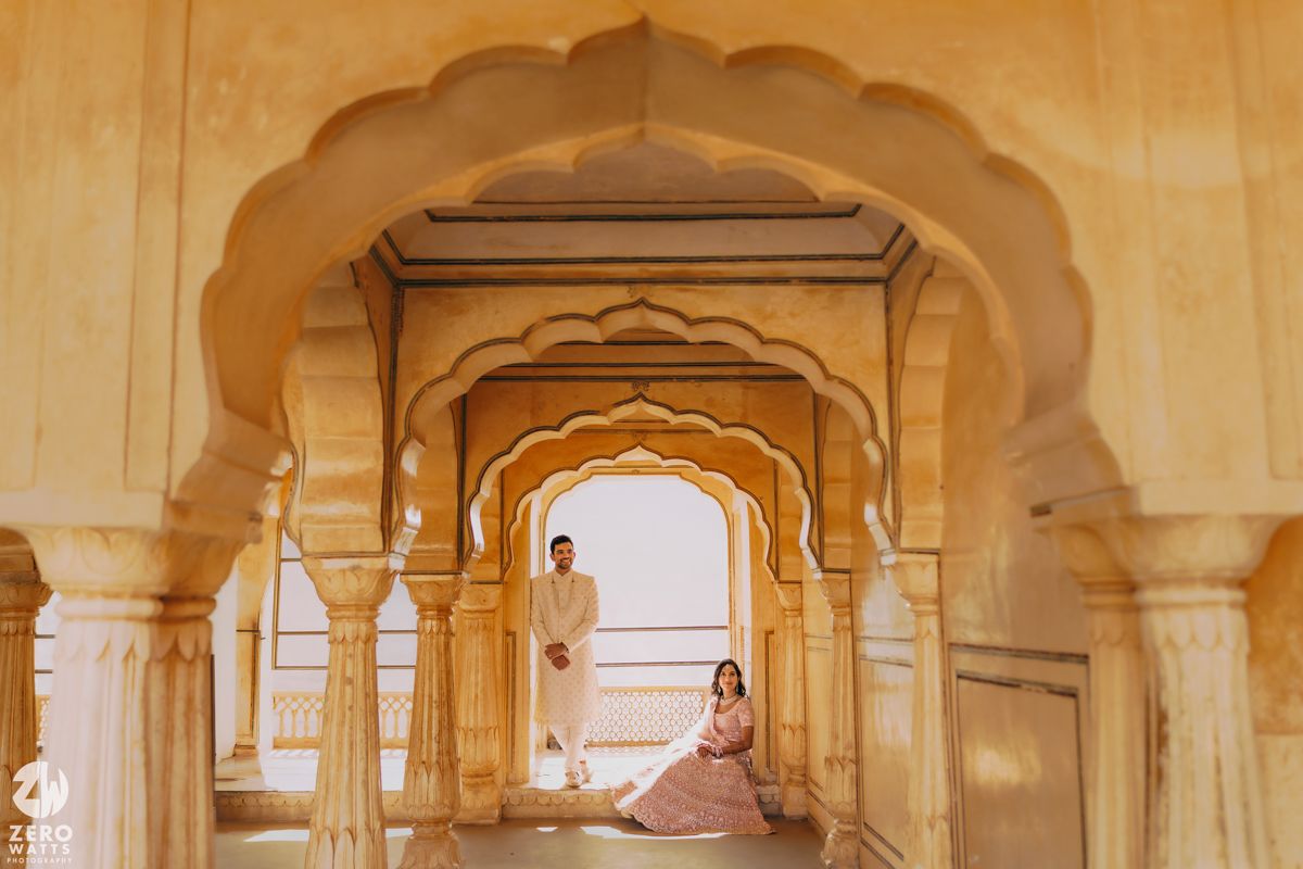 A person in traditional attire sits in an ornate archway corridor at Amber Fort in Jaipur, India.
