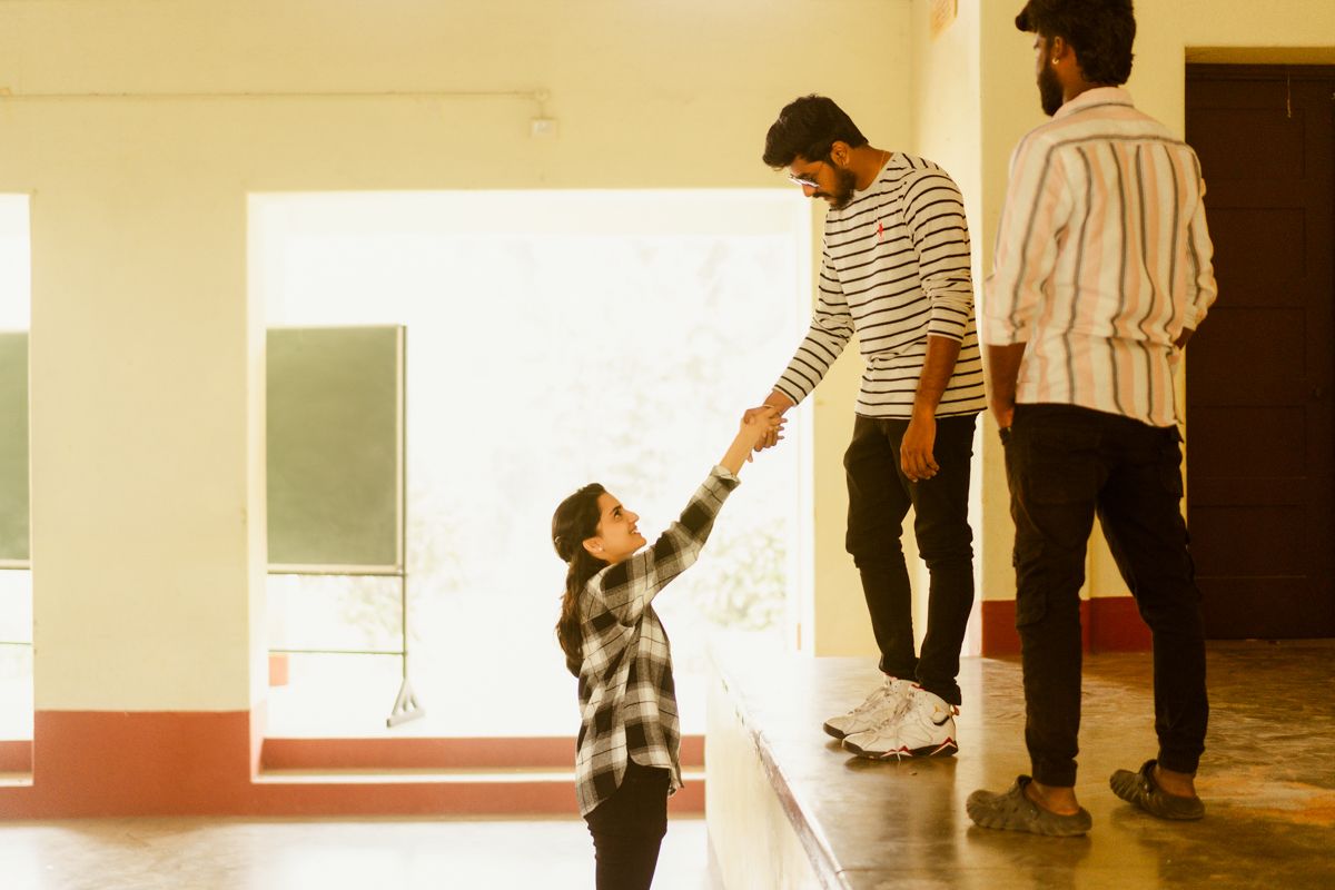 A small child in plaid reaches up to connect with someone wearing a striped shirt in a sunlit indoor space.