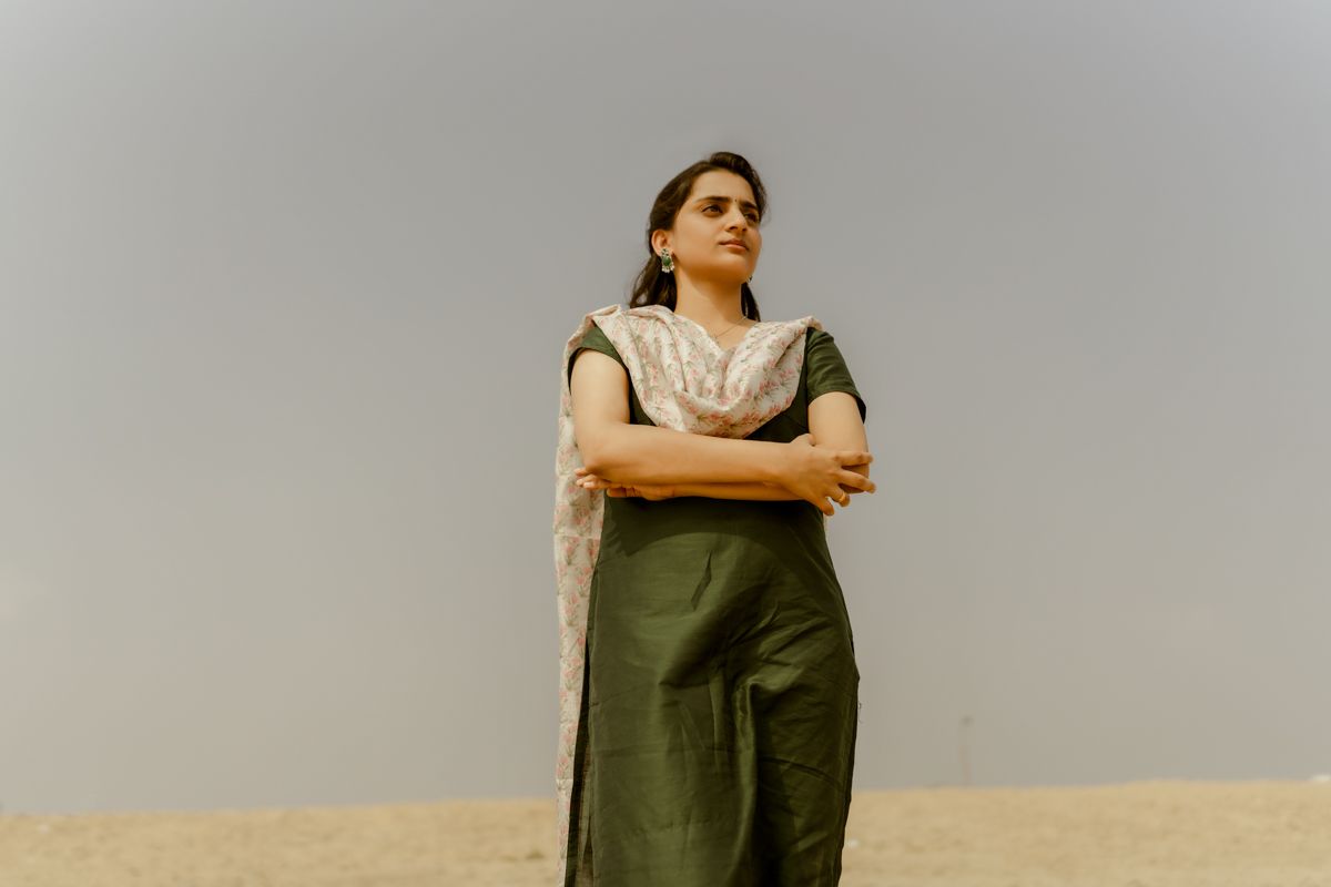 Person in casual attire standing confidently with crossed arms against a bright sky.