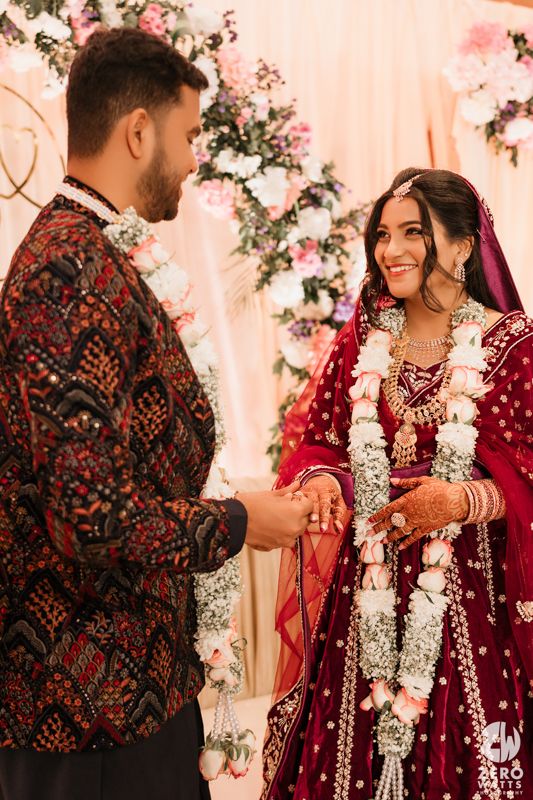 A couple in traditional wedding attire stand together amid floral decorations during their wedding ceremony.